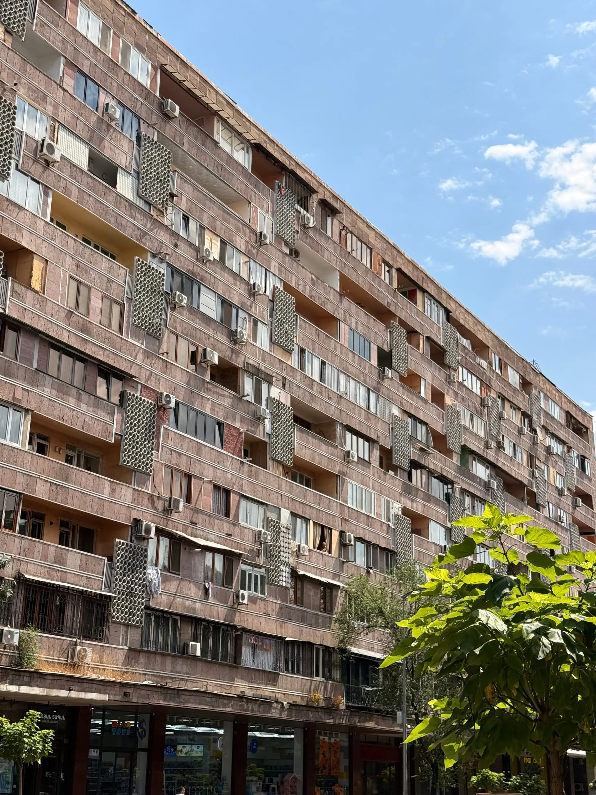 Looking up along the enormous facade of a Yerevan residential block, every balcony bay enclosed differently in glass, brick, sheet metal and grilles