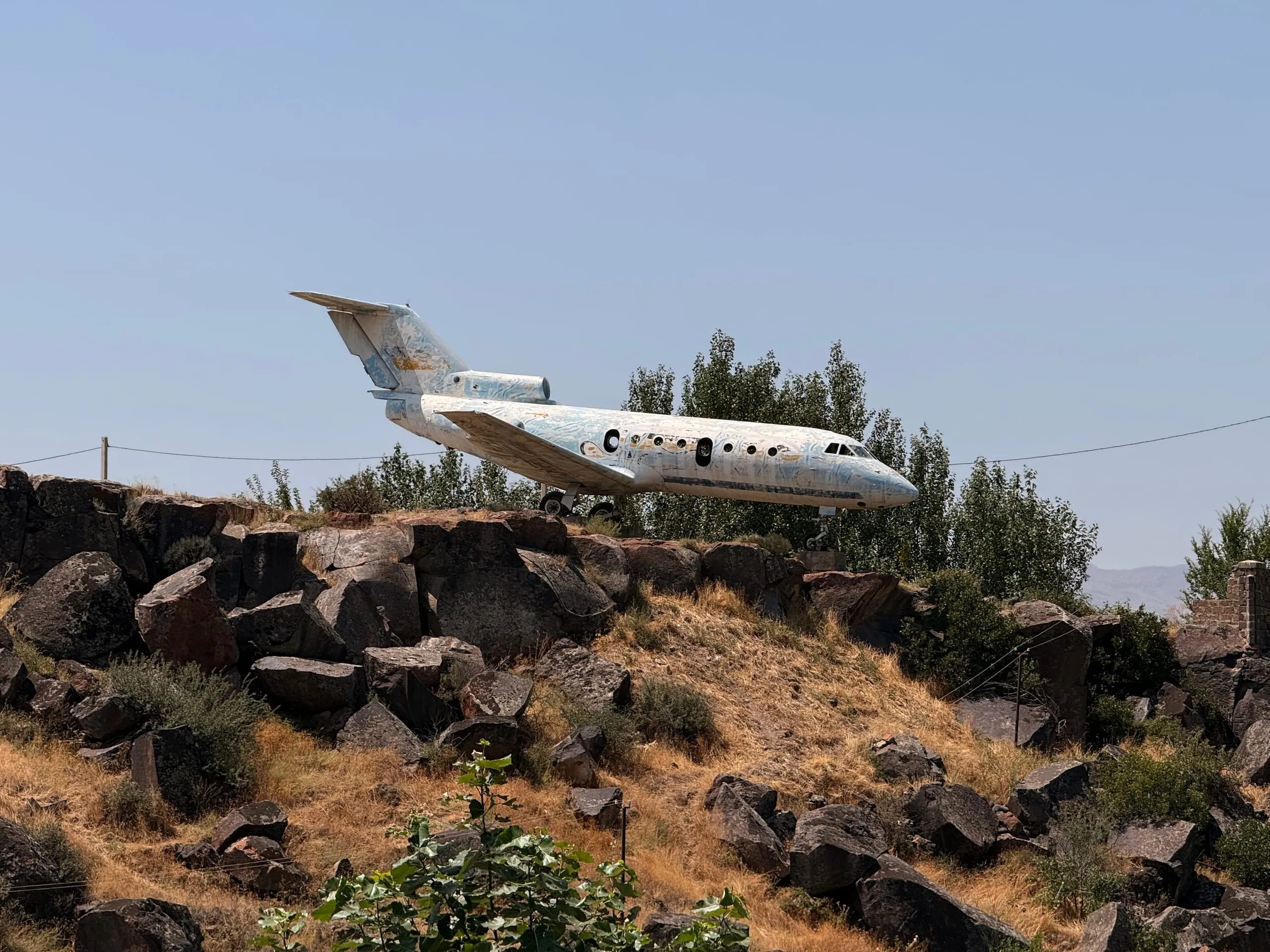 A Soviet Yak-40 passenger jet standing on concrete blocks on a shelf of black basalt above the Kasagh gorge, poplars behind it and no airport anywhere in sight