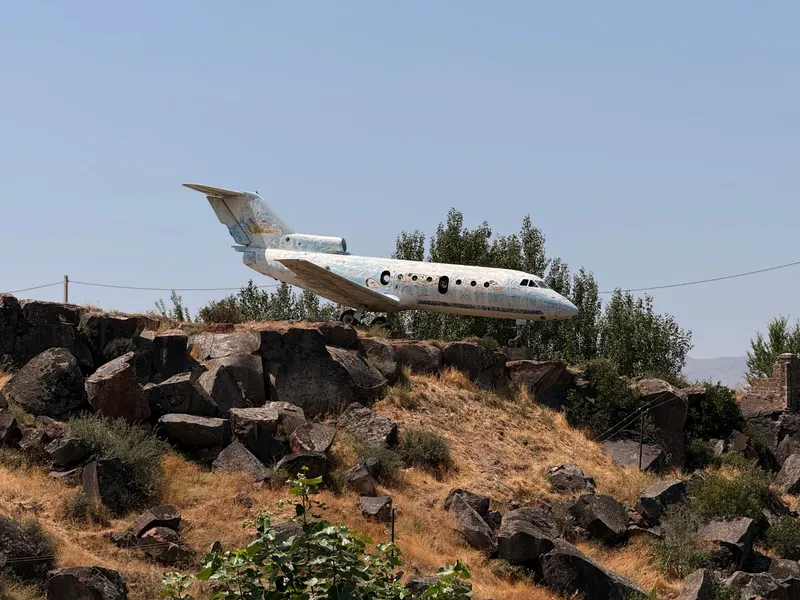 A Soviet Yak-40 passenger jet standing on concrete blocks on a shelf of black basalt above the Kasagh gorge, poplars behind it and no airport anywhere in sight