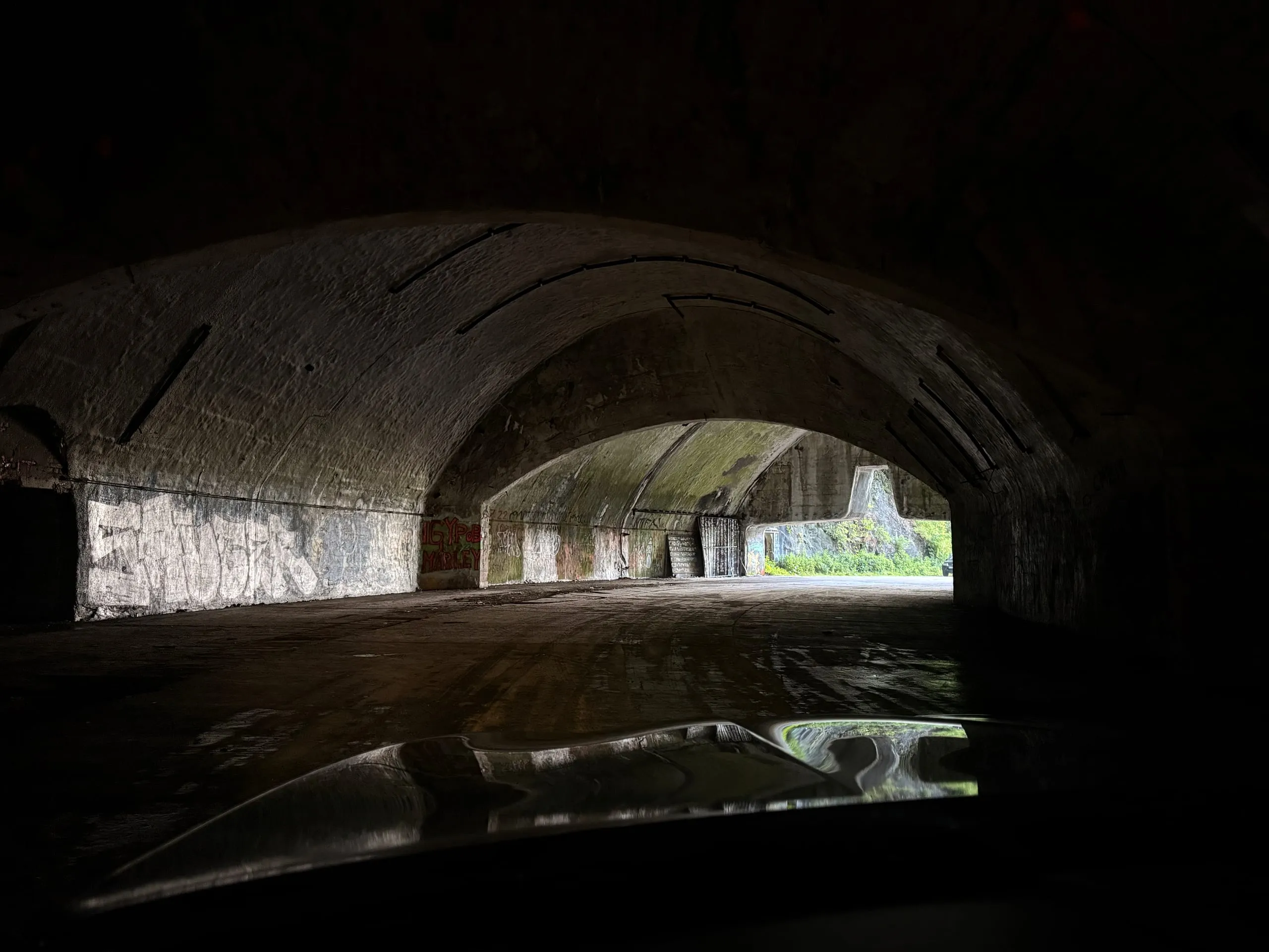 Driving into the mountain — the car's bonnet in the foreground, daylight in the tunnel ahead, inside an abandoned underground Yugoslav air base