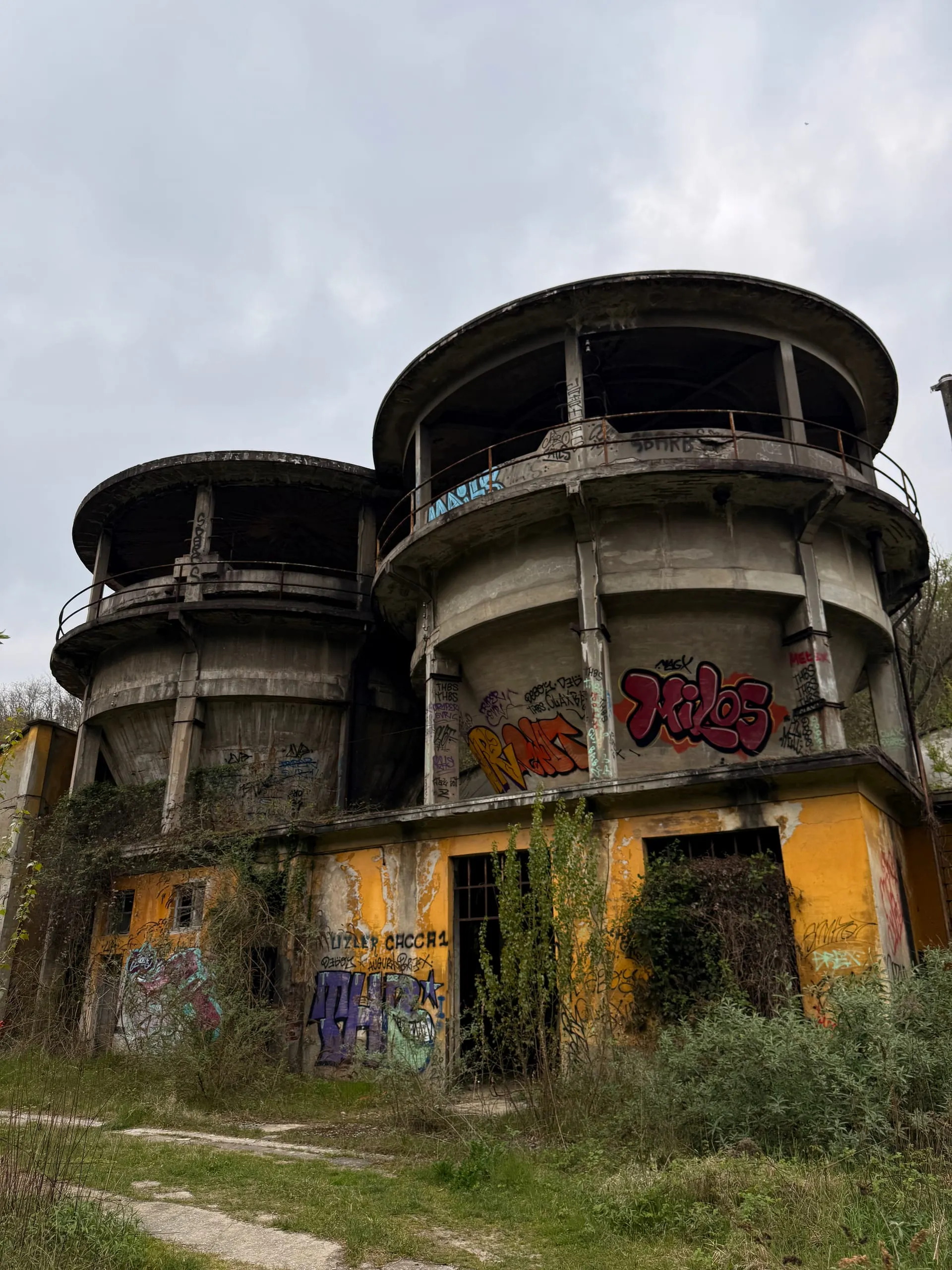 The twin graffiti-covered round towers of an abandoned paper mill, ivy climbing the ochre walls below them