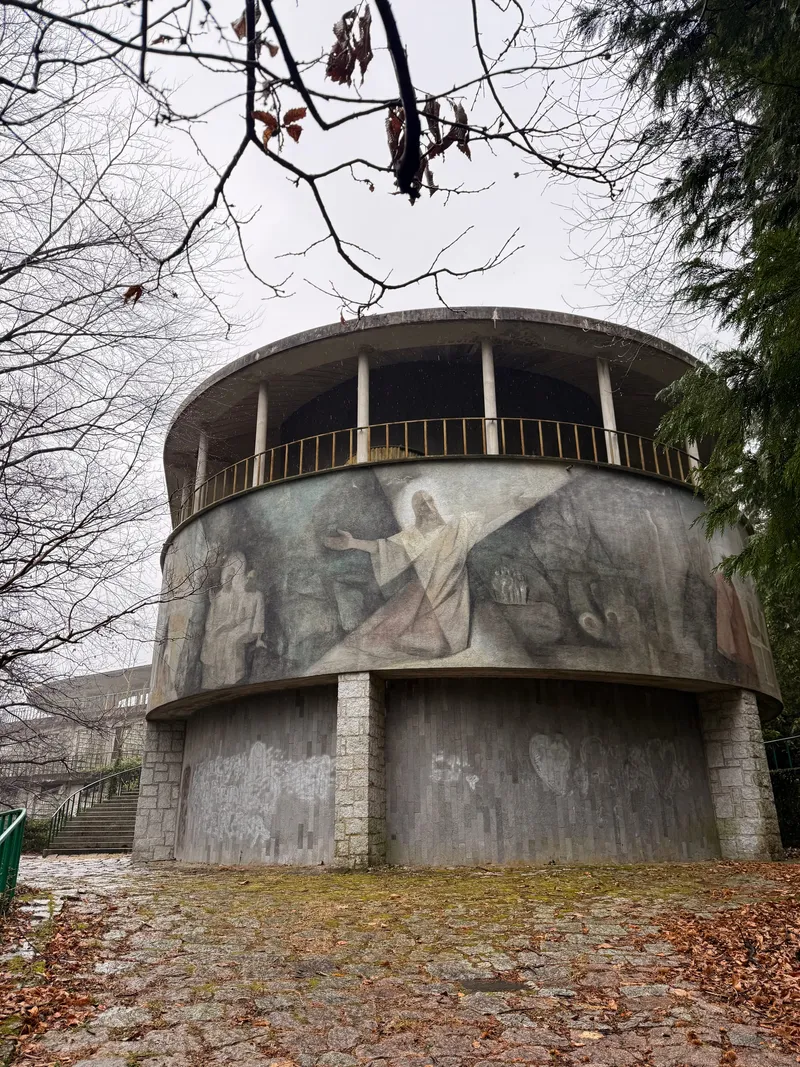 The circular concrete chapel of an abandoned modernist sanctuary, its facade bearing a faded mosaic