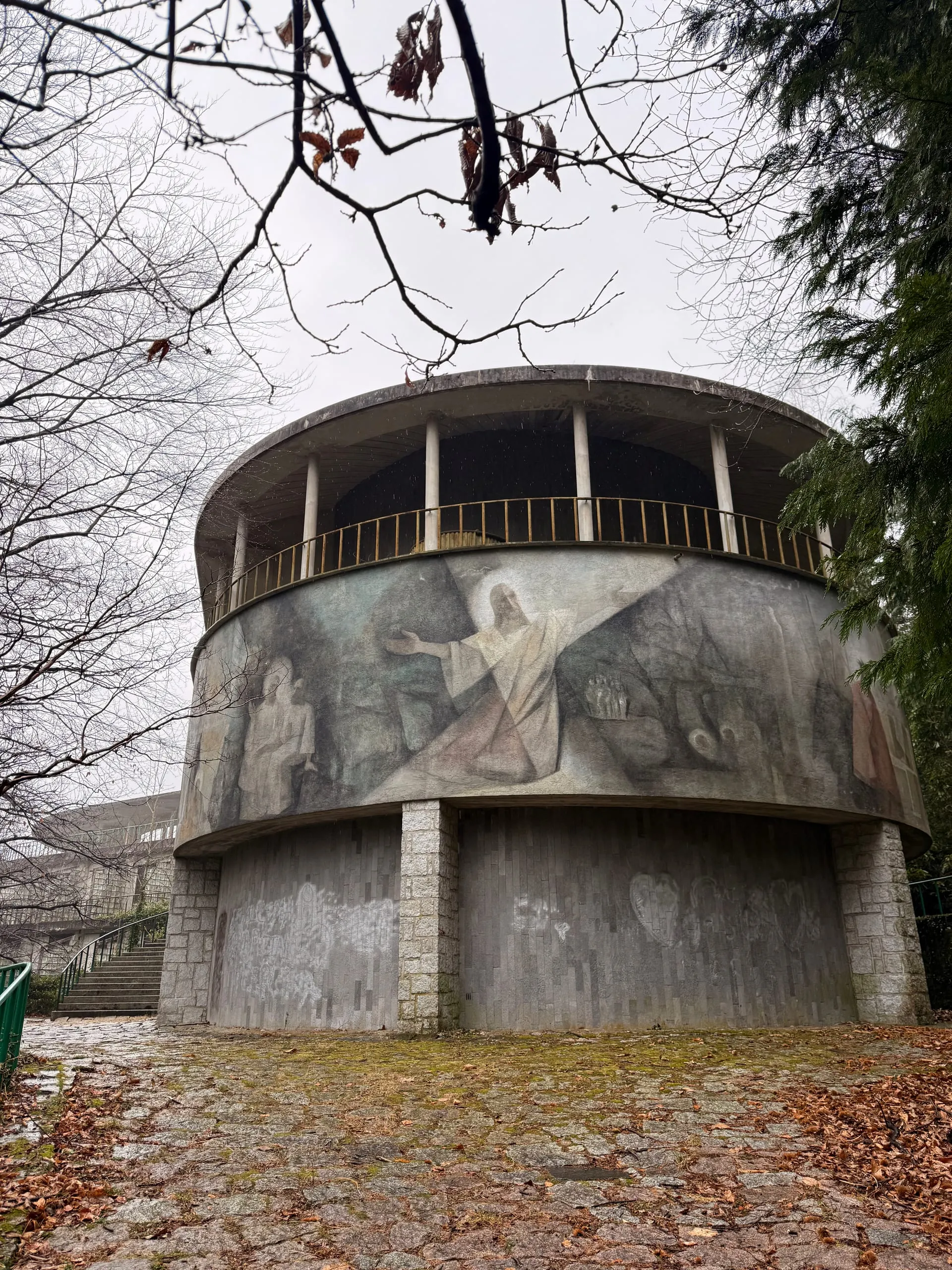 The circular concrete chapel of an abandoned modernist sanctuary, its facade bearing a faded mosaic