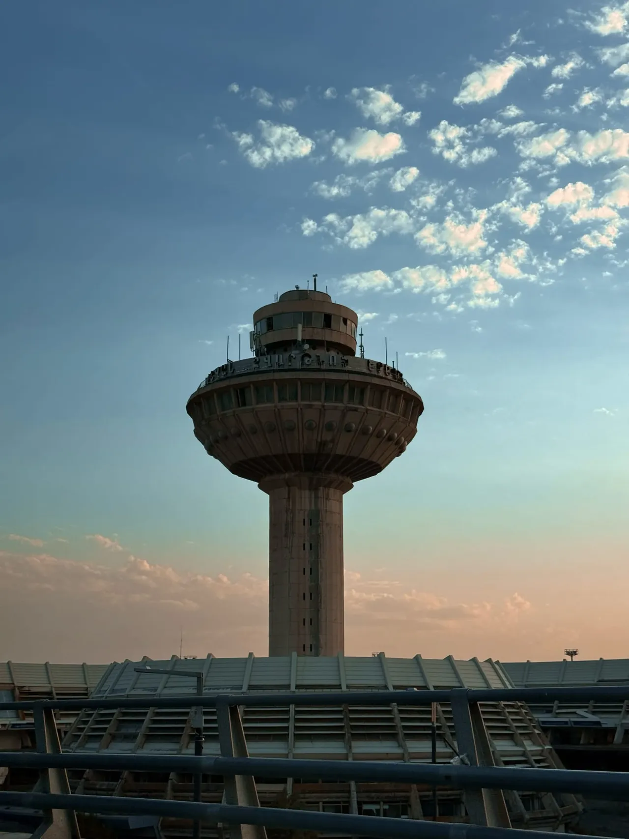 The flared concrete control tower at Zvartnots standing on a single stalk above the ribbed roof of the old round terminal, against a pale sunset sky