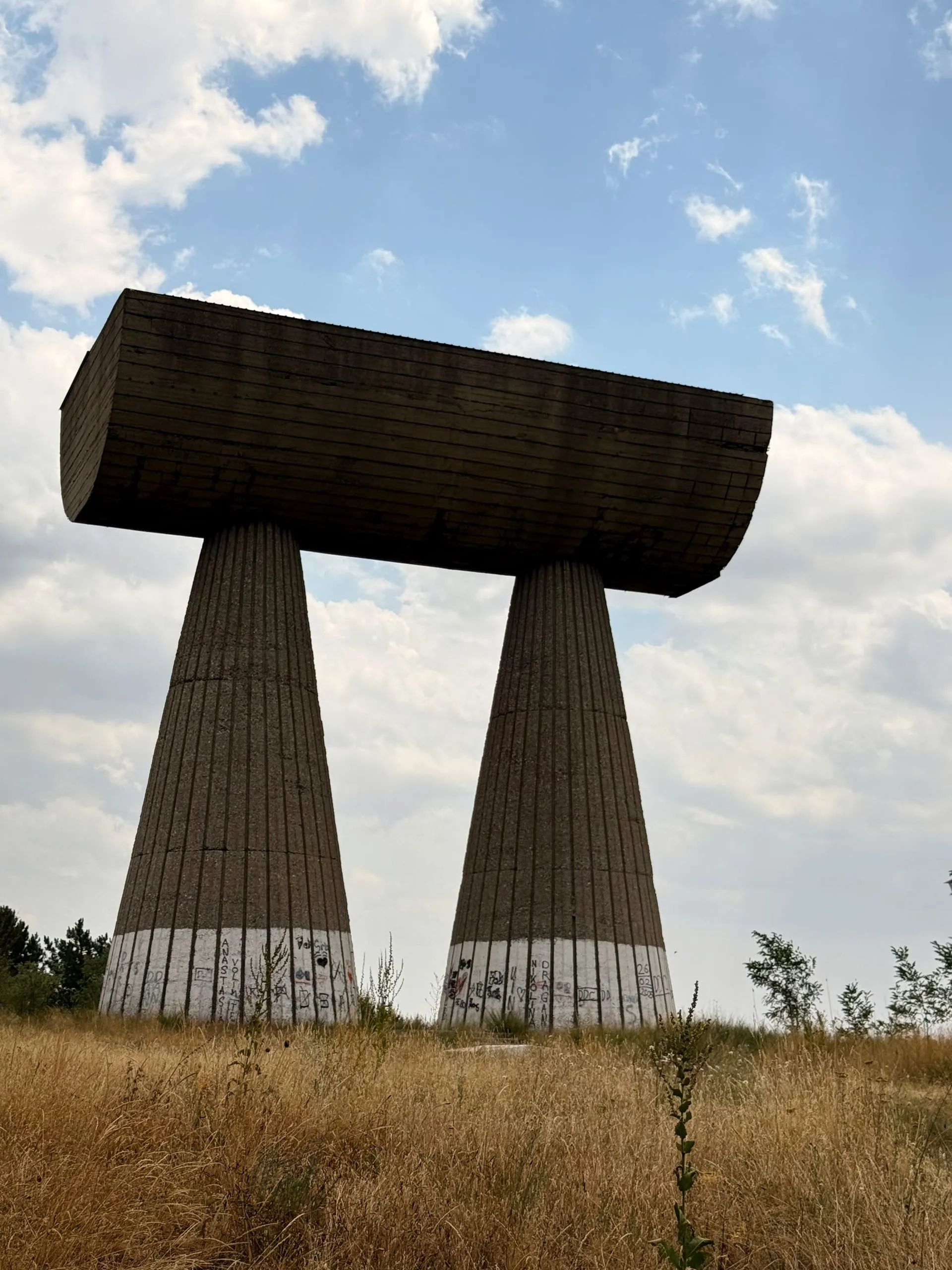 Two tapered concrete pillars carrying a horizontal drum, the miners' monument on the hill above Mitrovica