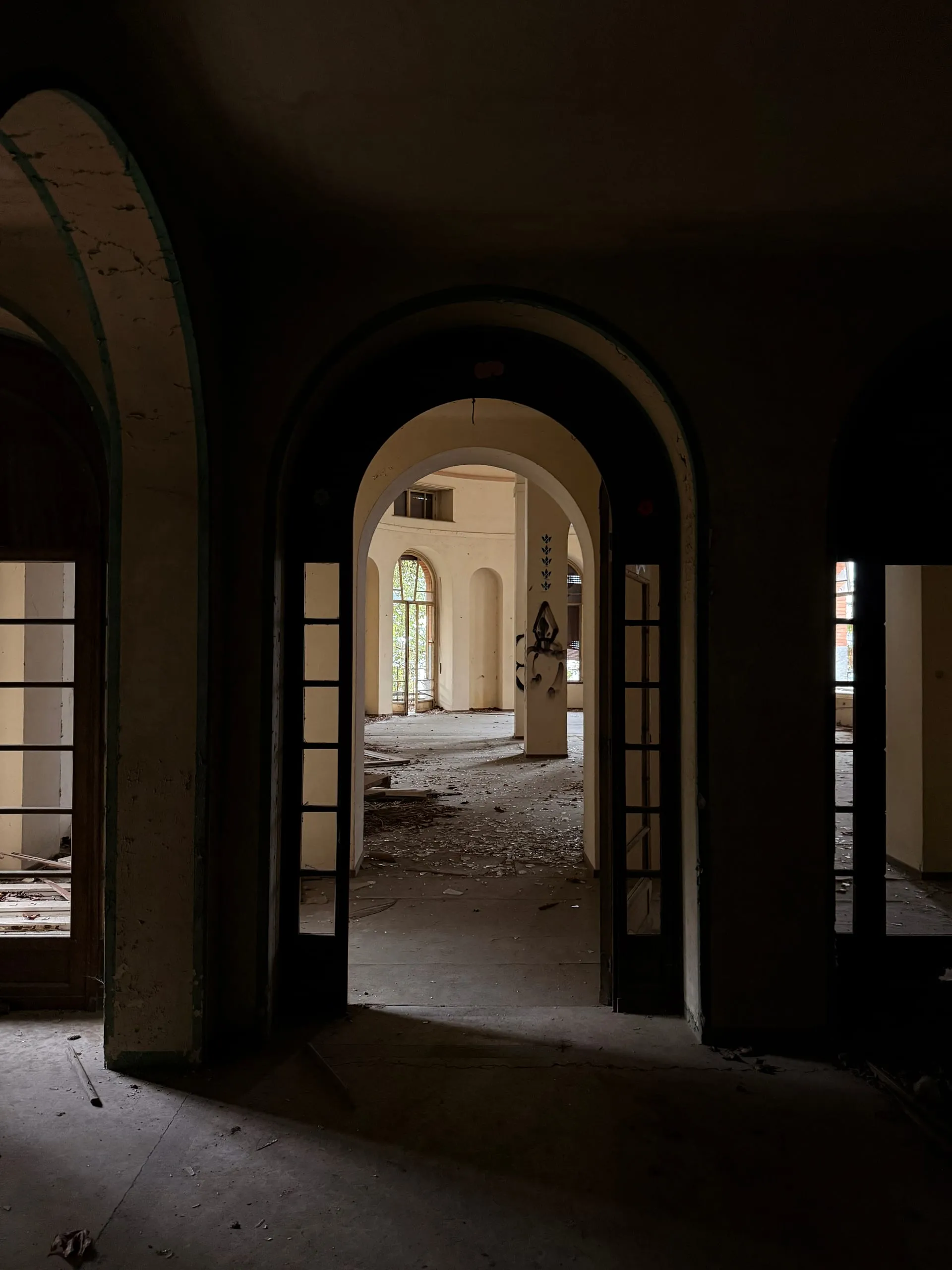 Layered arched doorways inside a vast abandoned children's holiday colony, opening onto a light-filled room