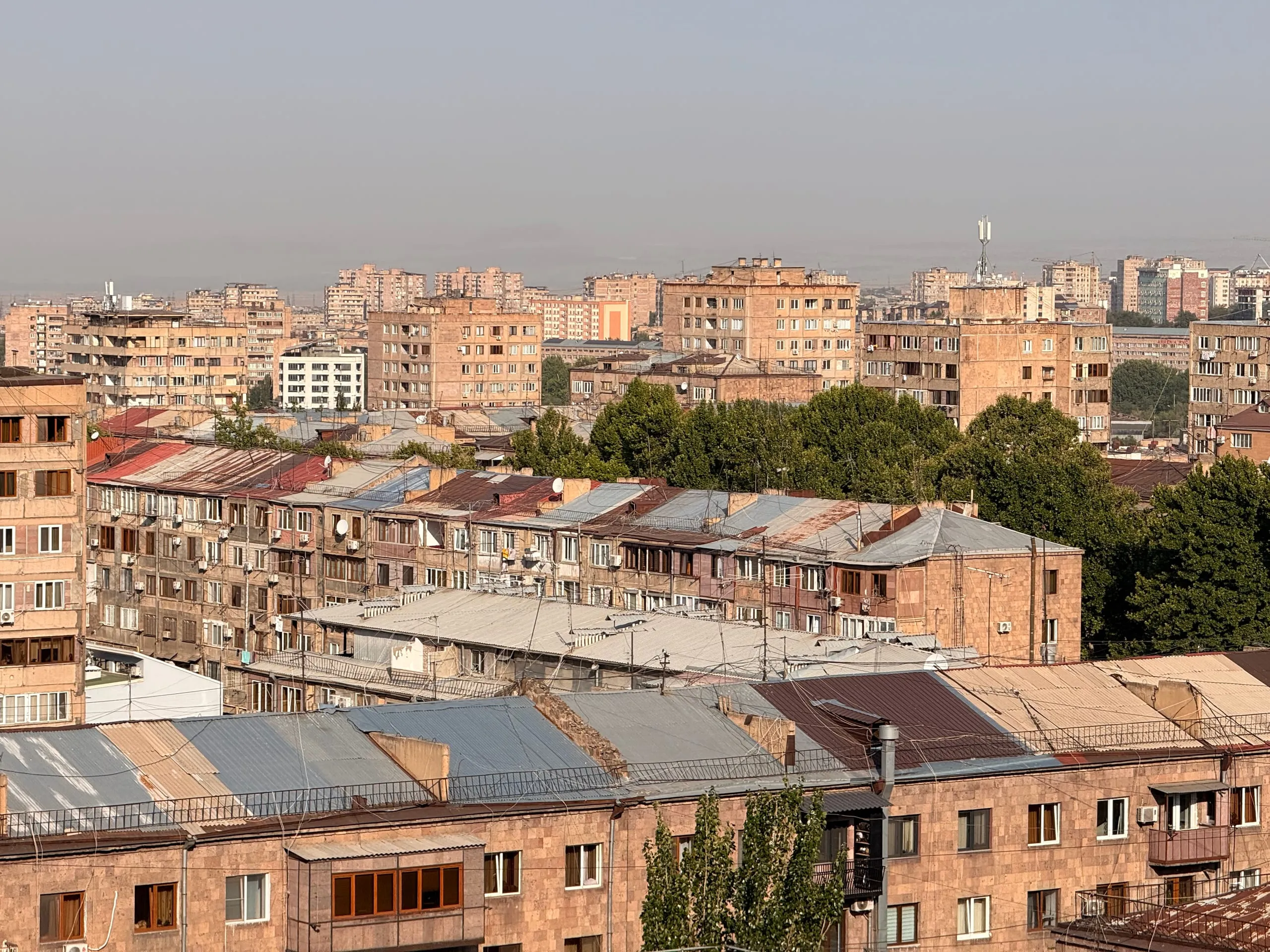 Yerevan roofs at half past eight in the morning — tuff blocks, corrugated iron, haze
